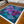 A framed floral art print featuring large purple orchids over a vivid blue and teal background, displayed on a wooden table in a living room setting.