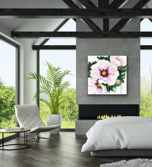 A square canvas wall art print featuring three light pink flowers with yellow centers and green leaves, displayed in a modern living room setting above a fireplace.