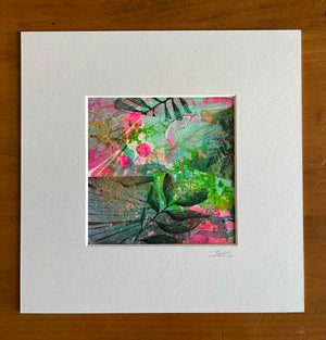 A matted abstract botanical art print featuring vibrant pink, green, and teal tones with leafy patterns, presented on a white mat board over a wooden surface.