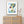 Framed abstract artwork above a rattan cabinet with decorative items.