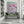 A large vertical canvas painting of pink peony flowers on a mint green background, displayed on a white wall above a green bench in a modern room with bookshelves and a window.