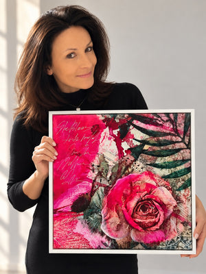 Edita Fields holding abstract floral canvas art print featuring a vibrant pink rose and pink brushstrokes with green leaves. Pink art in white floater frame.