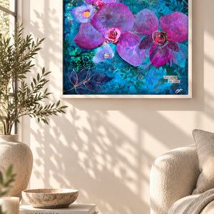 A framed square wall art print featuring large purple orchids and dragonflies on a vivid blue background, displayed in a styled living room above a sofa and next to a window.