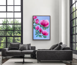 Luxury magnolia canvas print with pink flowers displayed above a modern grey sofa in a bright living room with large windows