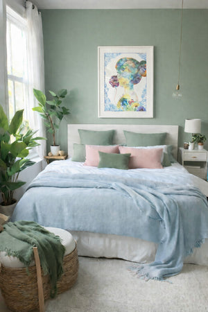 Framed colorful feminine portrait artwork displayed above a white bed in a softly styled bedroom with plants and natural light.