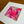 A square mixed-media art print featuring vibrant pink, red, and white butterfly and floral designs over a sheet music background, presented with a wide white mat board on a wooden table.