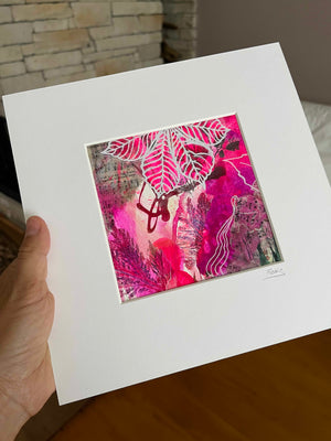 A hand holds a large white matted art print featuring an abstract painting with vibrant pink, magenta, and white leaf-like patterns and textured brushstrokes.