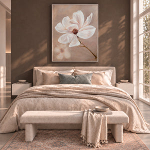 A styled bedroom interior with a large framed floral wall art piece above a bed. The artwork shows a white magnolia flower with a soft beige background.